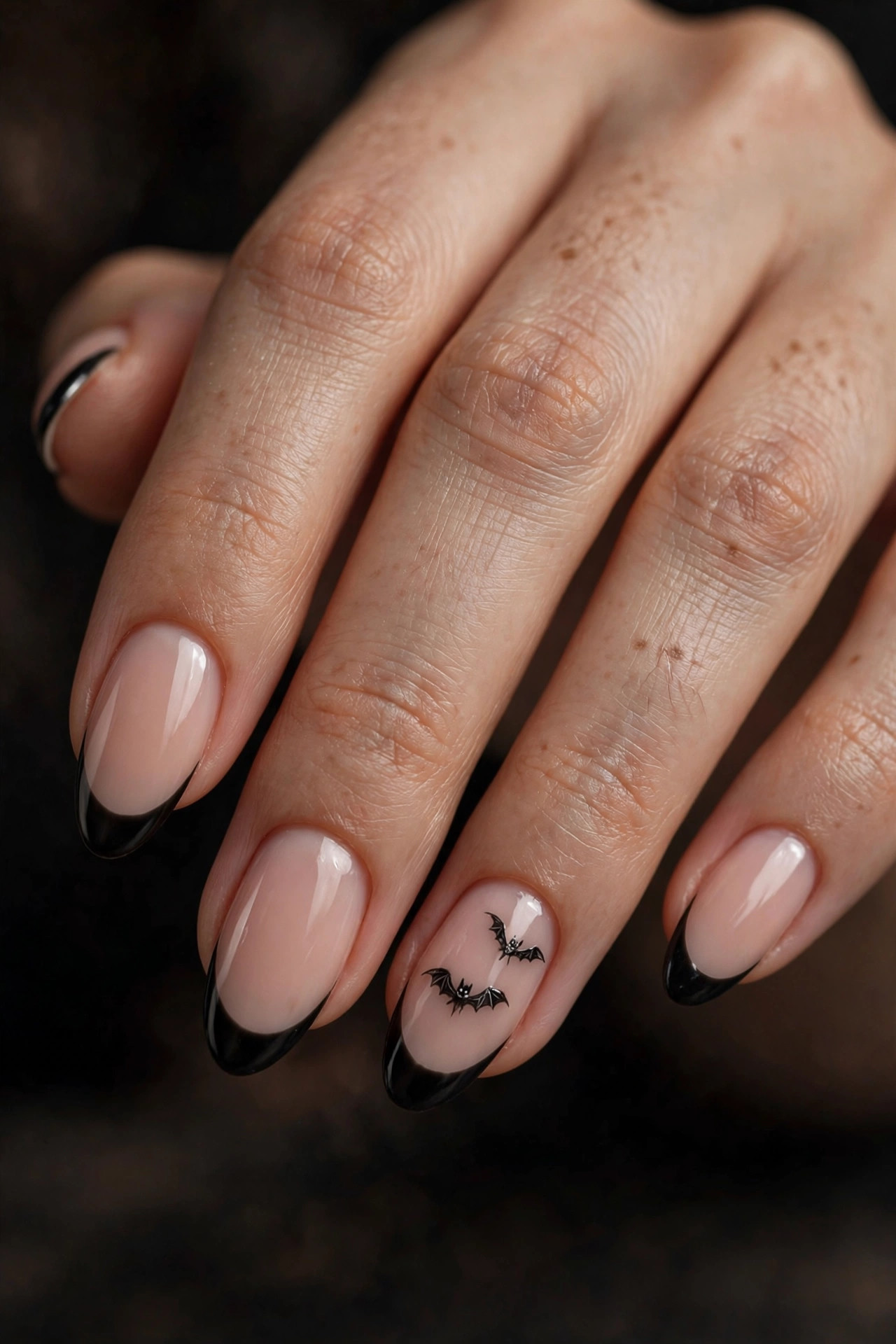 Nude almond nails with black French tips and tiny hand-painted black bats